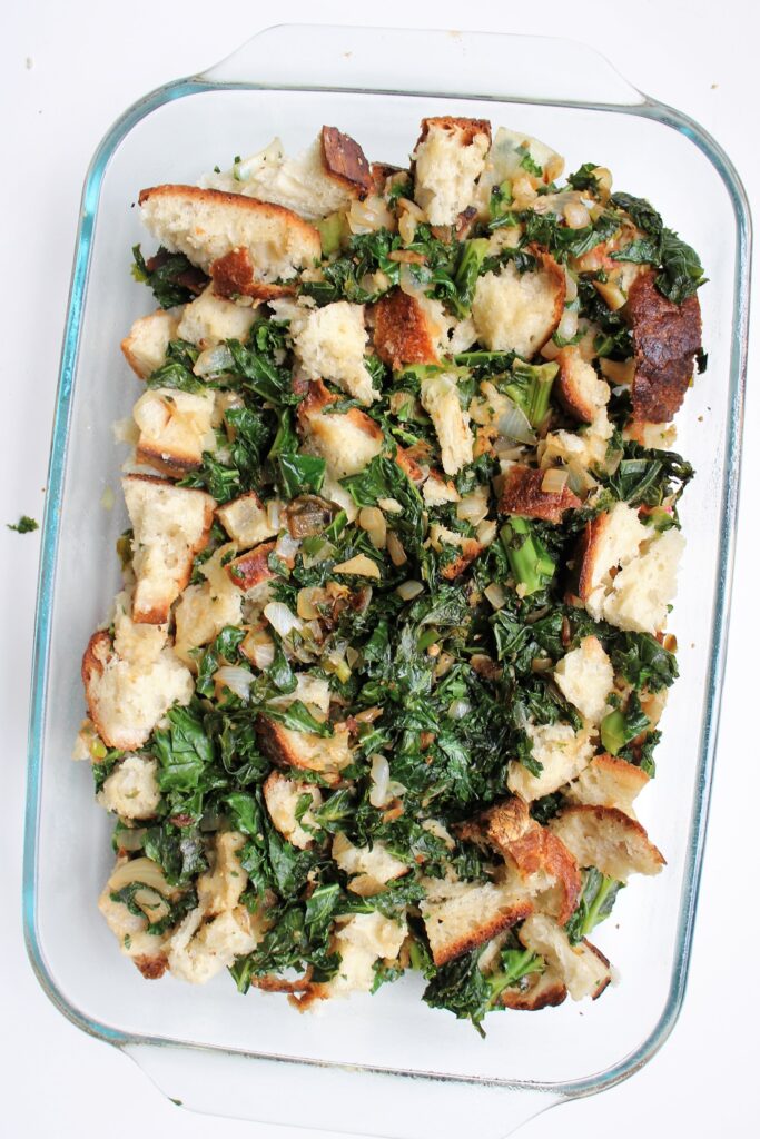 Bread cubs, kale, and cheese mixed together in a glass pyrex baking dish