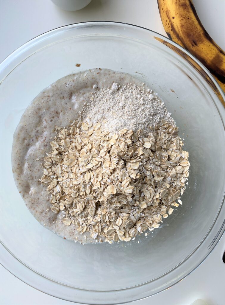 Rolled oats and oat flour on top of the wet ingredients in a glass bowl 