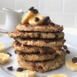Stack of 6 vegan banana pancakes on a plate with a white backsplash in the background
