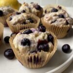 Close up of one gluten free lemon blueberry muffin on a plate with some blueberries on the side