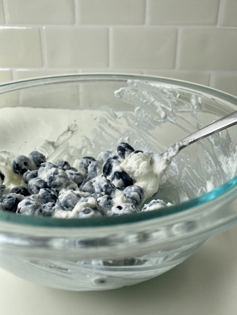 Glass Pyrex bowl full of blueberries coated in yogurt 