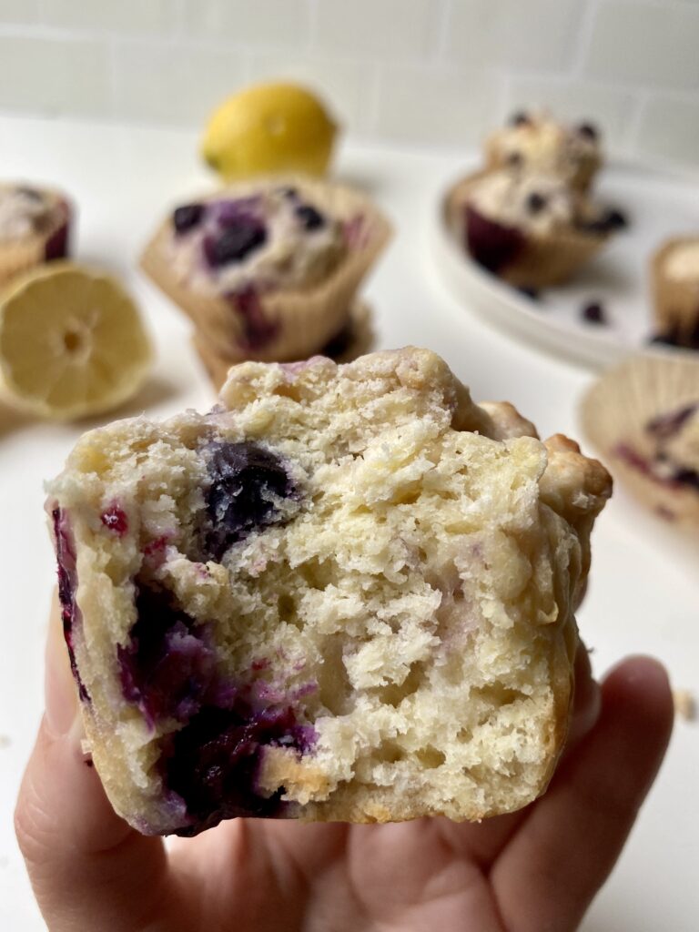 A close up of a blueberry lemon muffin that was bitten into, you can see the juice blueberry oozing out from the inside 