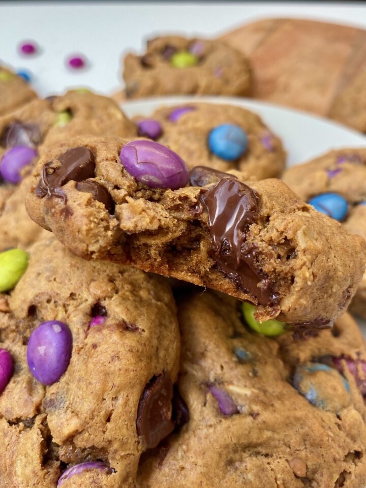close up of some gluten free monster cookies. the one on top is bitten into and chocolate is oozing out of it